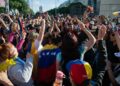 Vibrant crowd of Venezuelans celebrating with flags and cheers in an urban street setting.