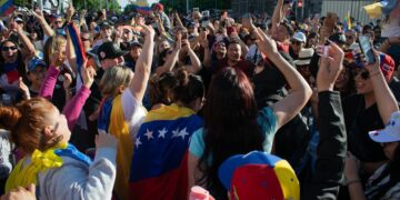 Vibrant crowd of Venezuelans celebrating with flags and cheers in an urban street setting.